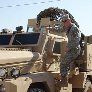 Jason Matheny holds onto the side of a Joint EOD Rapid Response Vehicle in Iraq.