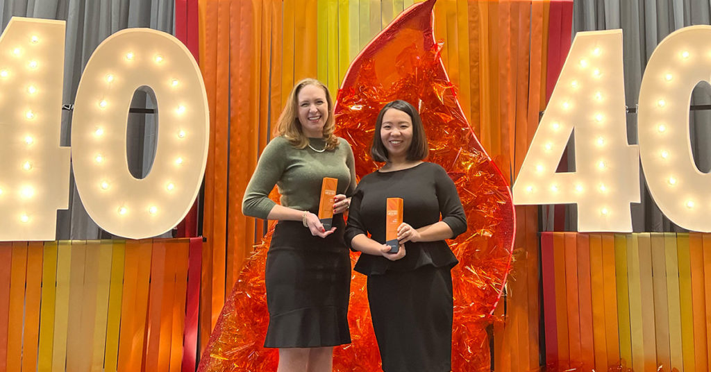 Alicia Swift and Fan Zhang standing in front of a 40 under 40 decoration while holding the awards they won