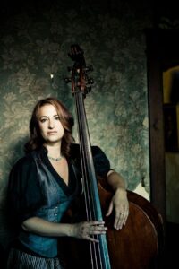 bryn davies sitting in front of a green wallpapered room with her cello